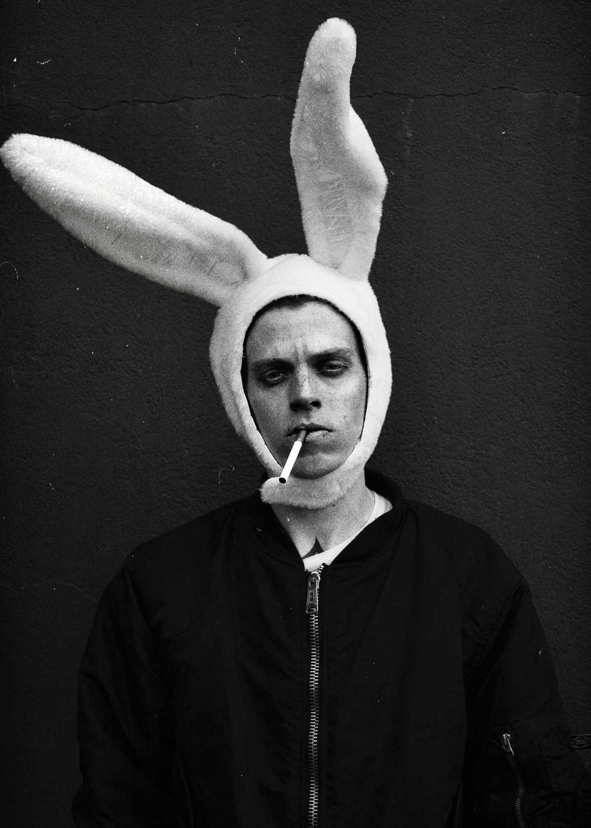 Una foto en blanco y negro de una persona con un sombrero de orejas de conejo, mostrando una expresión seria y sosteniendo un cigarrillo en la boca.